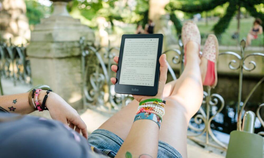 Mulher segurando dispositivo de leitura enquanto usa um app para ler livros grátis